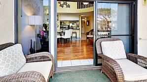 A modern home with a glass door leading to a dining area and kitchen. There are wicker chairs outside and a lamp inside. - Where Families Gather Kihei 2BR Loft Condo Heated Pool Hot Tub Near Beach (Kihei)