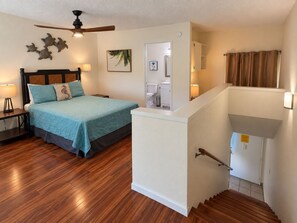 A bedroom with a bed, nightstand, and wall art. There is a staircase leading to an upper level. - Where Families Gather Kihei 2BR Loft Condo Heated Pool Hot Tub Near Beach (Kihei)