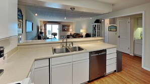 A modern kitchen with a dishwasher, double sink, and white cabinetry. - Terrapin Tides | Oceanfront + Community Pool! (Kure Beach)
