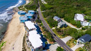 An aerial view of a coastal hotel with multiple buildings, a beach, and a road. - Terrapin Tides | Oceanfront + Community Pool! (Kure Beach)