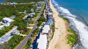 An aerial view of a coastal residential area with houses along a beachfront, a road, and a water tower in the distance. - Terrapin Tides | Oceanfront + Community Pool! (Kure Beach)