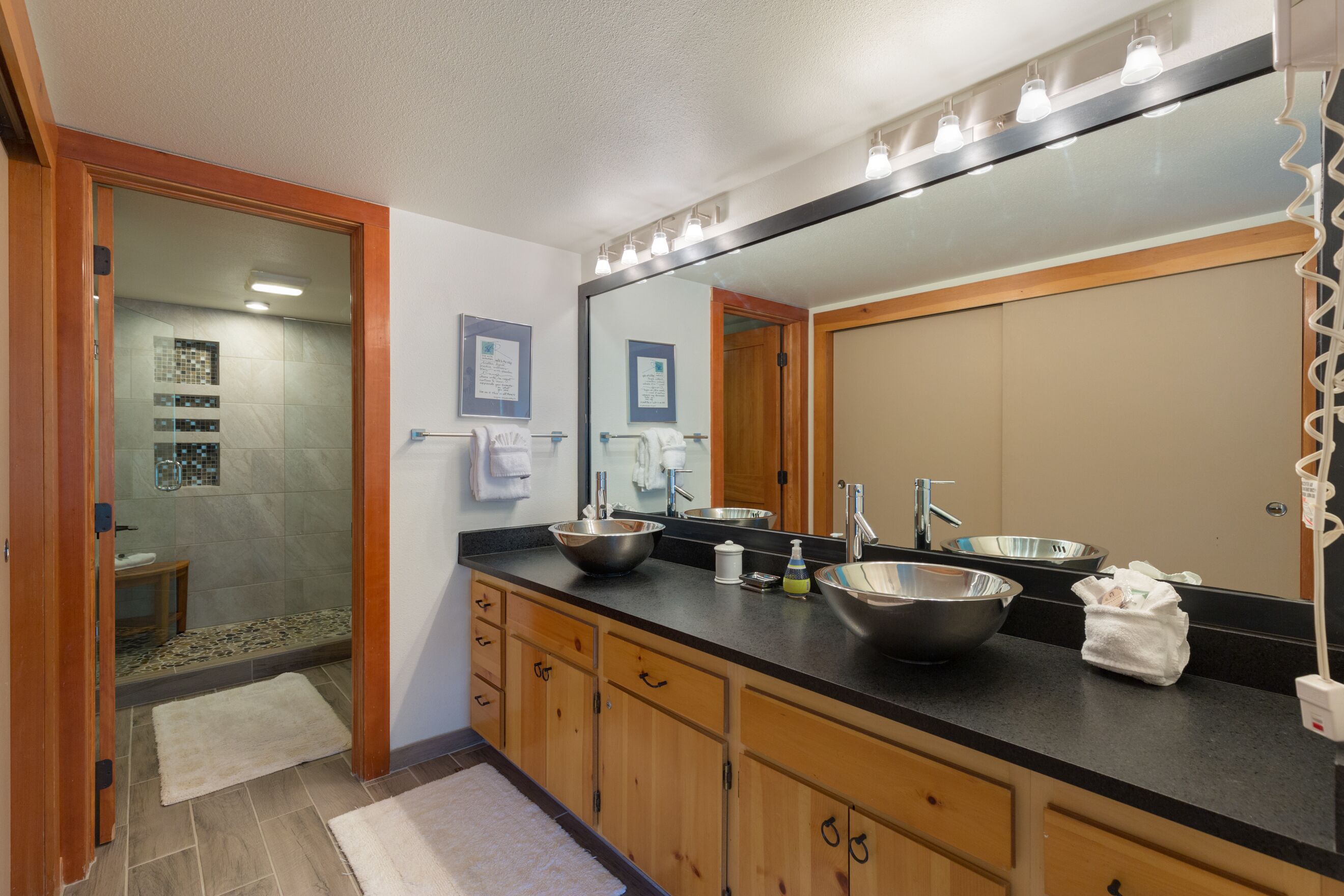 A bathroom with a large mirror, two sinks, and a shower area.