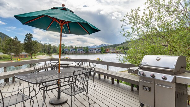 Eine Terrasse mit Gartenmöbeln, einem Grill und Blick auf See und Berge.