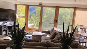 Ein Wohnzimmer mit großem Fenster, einer Couch, einem Couchtisch und zwei Zimmerpflanzen.
