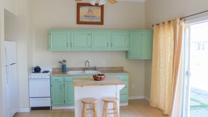 A kitchen with light green cabinets, a white stove, a sink, and two wooden stools. - Beach Odyssey (Saco)