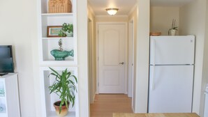 A narrow hallway with a white door at the end, a white refrigerator on the right, and a television on the left. - Beach Odyssey (Saco)
