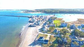 Ein Luftbild einer Küstenwohngegend mit Häusern direkt am Strand, einer Marina mit Booten und freiem Blick auf den Ozean.