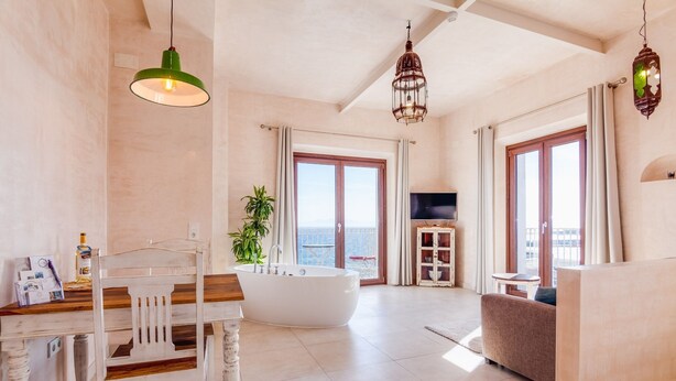 A spacious living room with a large window, a bathtub, and a dining area with a wooden table and chairs.