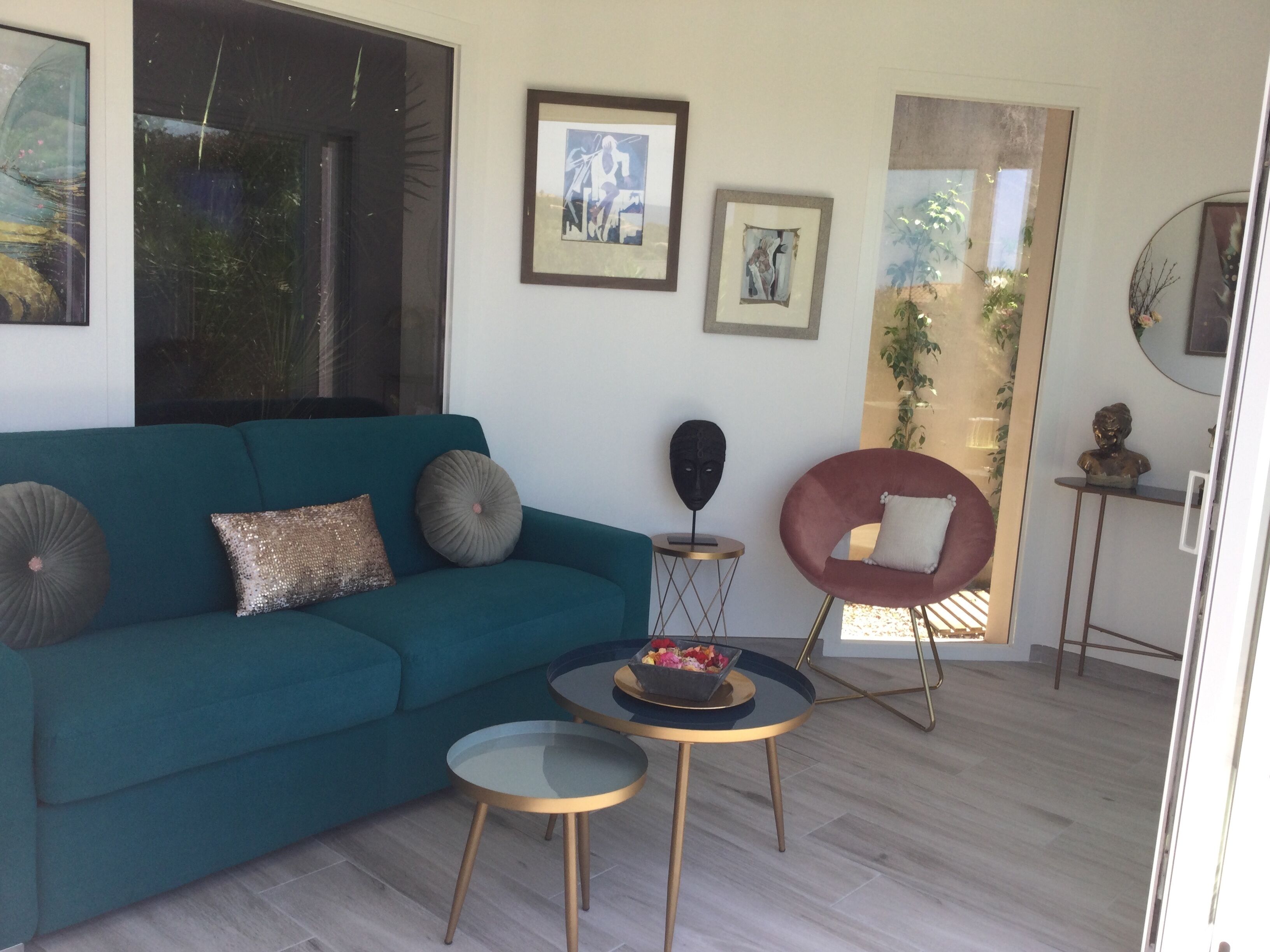 A modern living room with a teal sofa, two round tables, and a red chair.