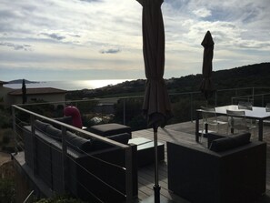 A terrace with outdoor furniture, a view of the sea, and a mountainous landscape.