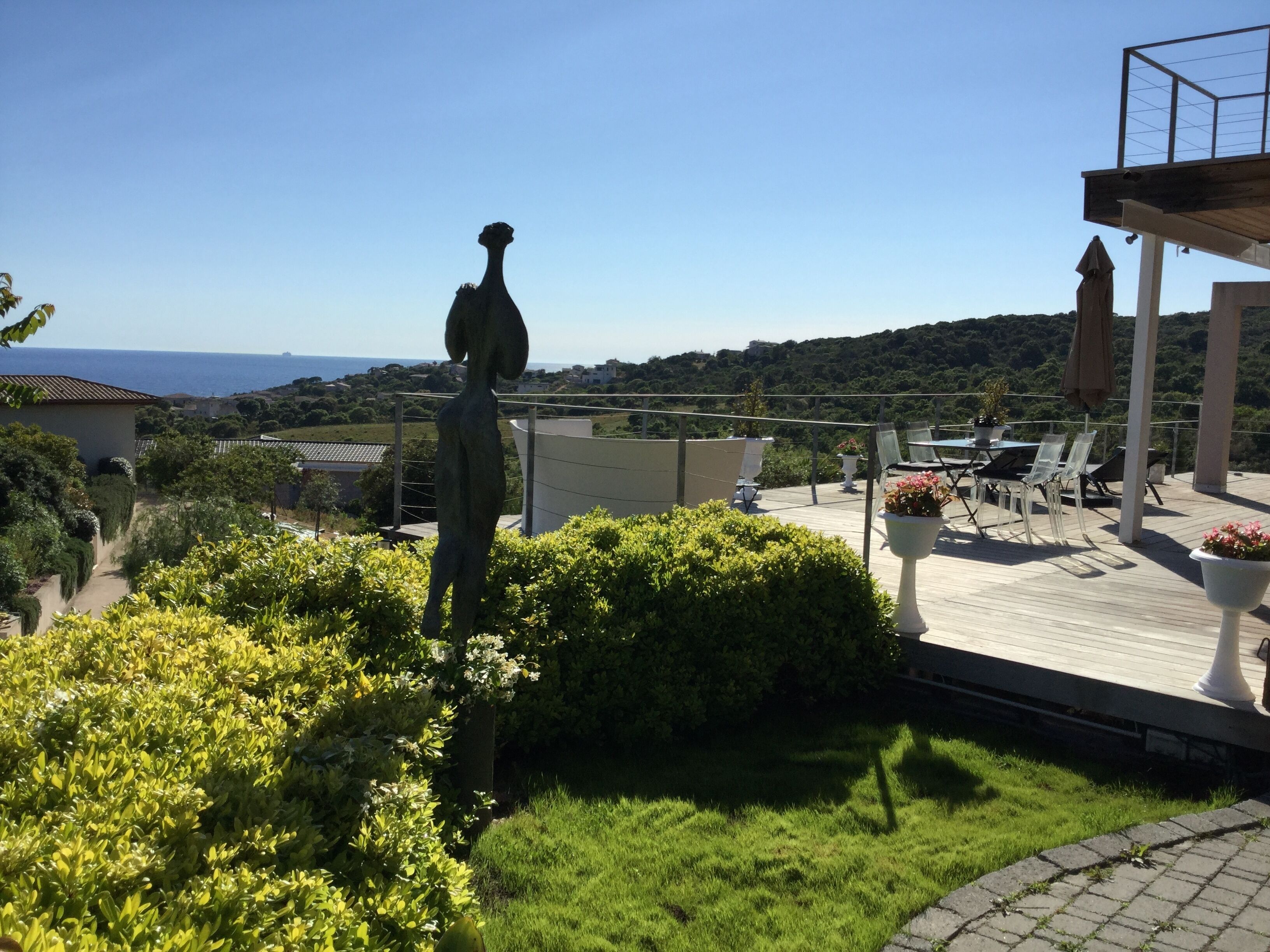 A rooftop terrace with a statue, outdoor seating, and a view of the sea and hills.