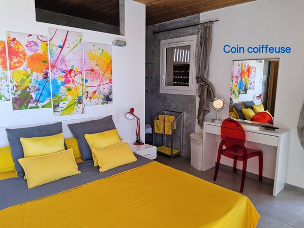 A bedroom with a bed, a desk, a chair, a mirror, and abstract art on the wall.