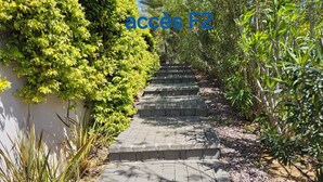Ein gepflasterter Weg führt zu einer Treppe aus Stein, umgeben von üppigem Grün.