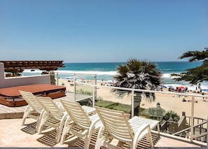 Uitzicht op het strand vanaf een balkon met witte stoelen en een houten terras.