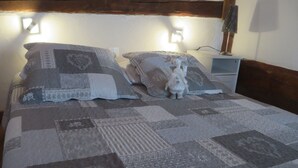 Ein Bett mit Patchwork-Quilt, zwei Kissen, eine kleine weiße Figur und ein Nachttisch mit Lampe.