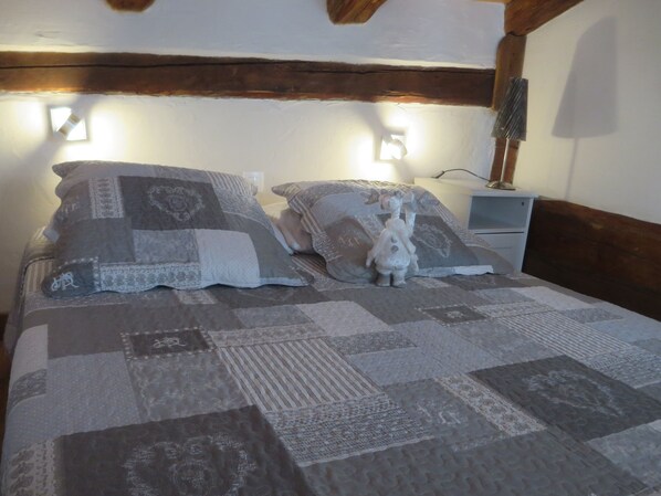 Een bed met een lappendeken, twee kussens, een kleine witte beeldje en een nachtkastje met een lamp.