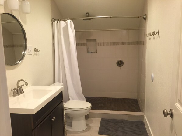 A bathroom with a toilet, a shower with a glass door, a sink, and a mirror. - Fresh bed and fresh bread in beautiful studio! (Mesa)