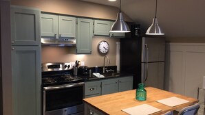 Uma cozinha compacta com armários azul-claros, eletrodomésticos de aço inoxidável, uma mesa de madeira e iluminação pendente.