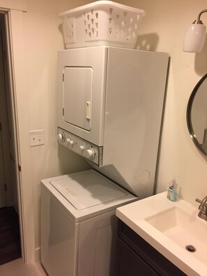 Een kleine wasruimte met een wasmachine en droger, een wit wasbakje en een fles handzeep.