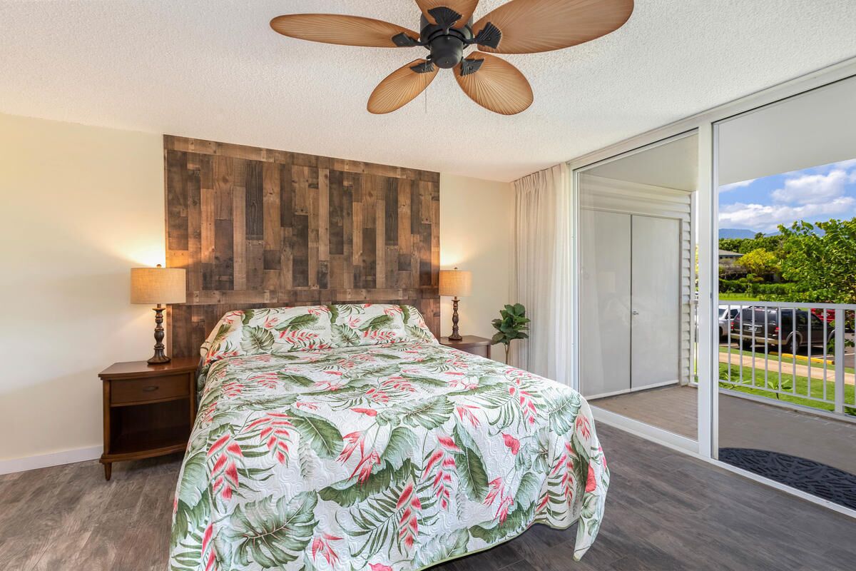 A bedroom with a bed, a ceiling fan, a nightstand, a lamp, and a view of the outdoors.