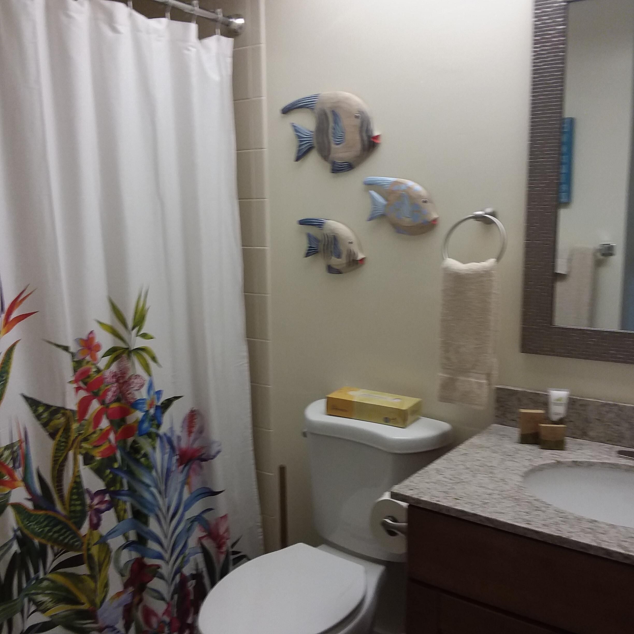 A bathroom with a toilet, a sink, a shower curtain, and decorative fish on the wall.
