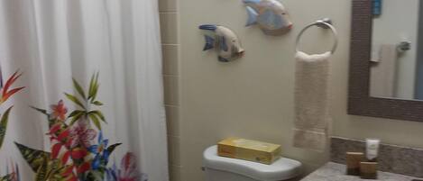 A bathroom with a toilet, a sink, a shower curtain, and decorative fish on the wall.