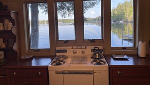A kitchen with a stove, three windows overlooking a lake, and a 'Welcome to the Lake' sign. - Adirondack Beauty! 110 ft Lake Frontage On Brant. Lake - Beach; Kayaks, Canoes (Greig)