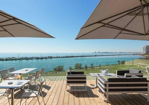 Enjoy a serene waterfront view from our outdoor terrace, featuring comfortable seating and umbrellas.