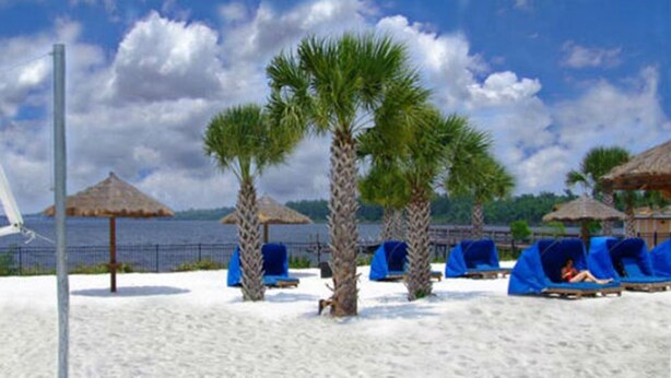 Une plage avec un filet de volley-ball, des palmiers et des chaises longues placées sous des parasols en feuilles de palmier.