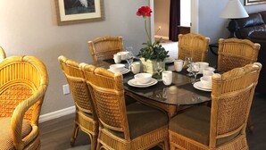 Un coin repas avec une table ronde dressée pour six personnes, entourée de chaises en osier.