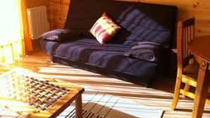 Une pièce chaleureuse avec un canapé aux couleurs sombres, un coussin à carreaux, une table en bois et une chaise.