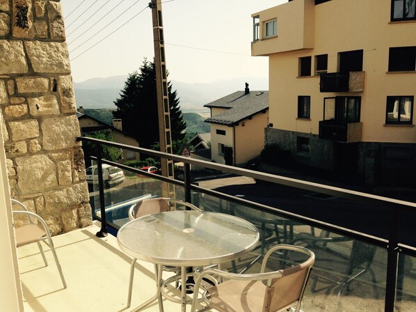 A balcony with a glass table and chairs, overlooking a street with buildings and a distant view of mountains. - 5-minute walk from the gondolas, bright T3, sleeps 8, free wifi. (Font-Romeu-Odeillo-Via)