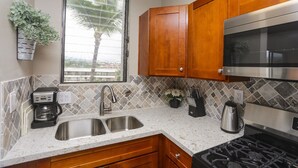 Una cocina con gabinetes de madera, un lavamanos de acero inoxidable, una cafetera y un microondas.