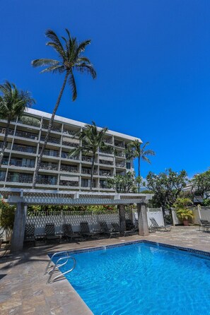 A hotel with a pool, palm trees, and a clear blue sky.