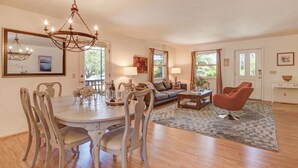 A dining area with a round table, chairs, and a chandelier. There is a sofa and a coffee table in the living area.