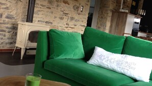 Una habitación acogedora con un sofá verde, una mesita de madera con un vaso de bebida verde y una almohada blanca con texto.
