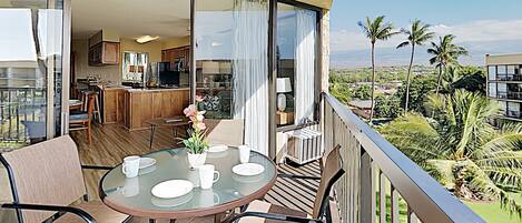 A balcony with a table and chairs, a ceiling fan, and a view of a lush landscape with palm trees.