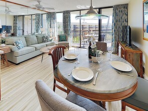 Un coin repas avec une table ronde pour quatre personnes, un canapé et un balcon avec des sièges d’extérieur.