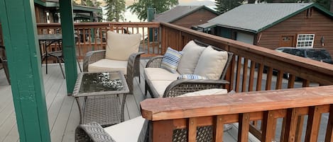 Una terraza de madera con mobiliario de mimbre, que incluye un sofá y sillas, además de una mesa.