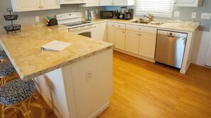 Una cucina con mobili bianchi, un forno a microonde, un fornello, una lavastoviglie e una finestra con persiane.