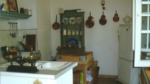 Een keuken met een fornuis, wastafel, planken met servies en hangende pannen.