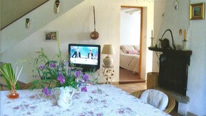 Een gezellige woonkamer met een televisie, een tafelkleed met bloemenmotief en een bed op de achtergrond.