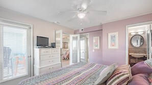 A bedroom with a bed, dresser, ceiling fan, and a bathroom with a sink and mirror.