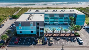 A multi-story hotel with a rooftop pool, located near a beach with a view of the ocean.