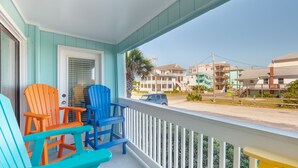 A porch with colorful Adirondack chairs, a white railing, and a view of a street with buildings.