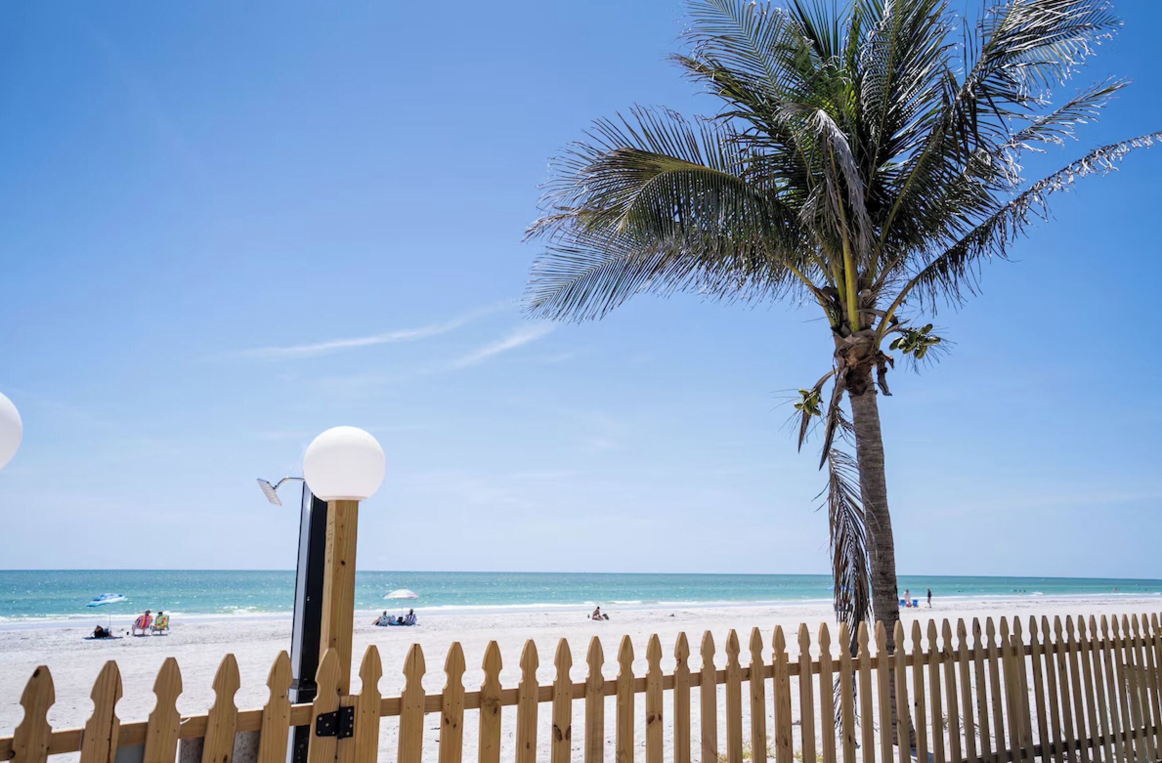 Ein Strand mit einer Holzzaun, einer Palme und blauem Himmel.