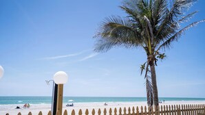 Une plage avec une clôture en bois, un palmier et un ciel bleu clair.