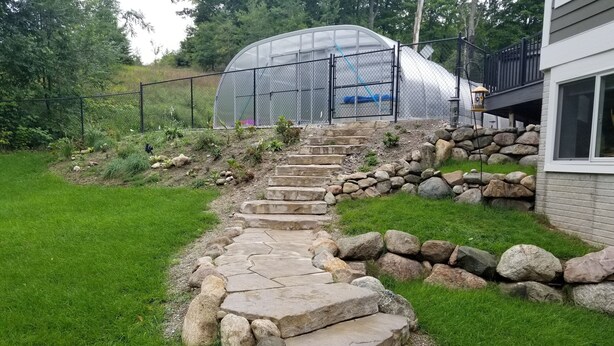 A stone staircase leading to a greenhouse, surrounded by a stone wall and a grassy area. - Elegant 2 King Bedroom Apt - 2 night minimum - 4 adults  (Traverse City)