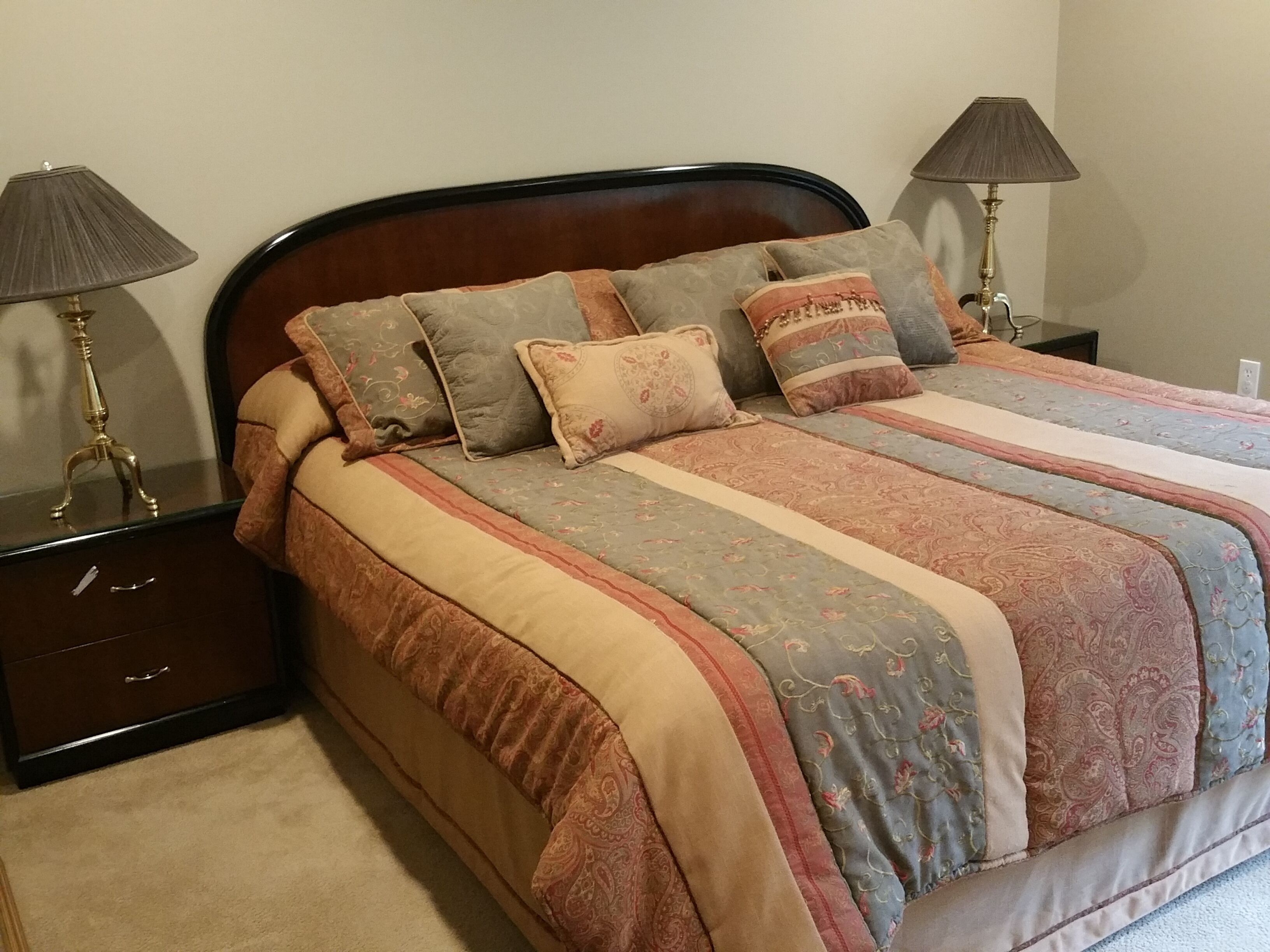 A neatly made bed with a patterned bedspread and multiple pillows, flanked by two bedside tables with lamps.