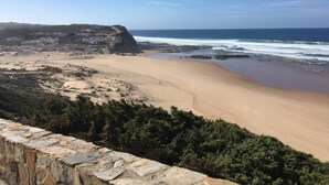 A coastal landscape with a sandy beach, rocky cliffs, and a stone wall.